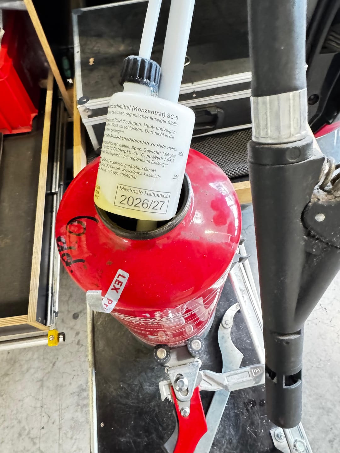 Nahaufnahme: Ein geöffneter Feuerlöscher wird mit Löschmittel-Konzentrat befüllt; die Flasche zeigt das Haltbarkeitsdatum.