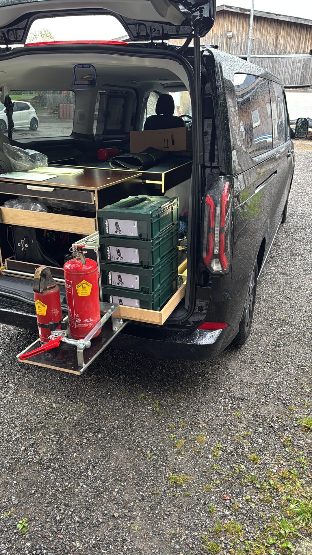 Heckansicht des Servicebusses mit ausgezogener Arbeitsplatte, darauf zwei Feuerlöscher in der Halterung und Werkzeugkoffer.