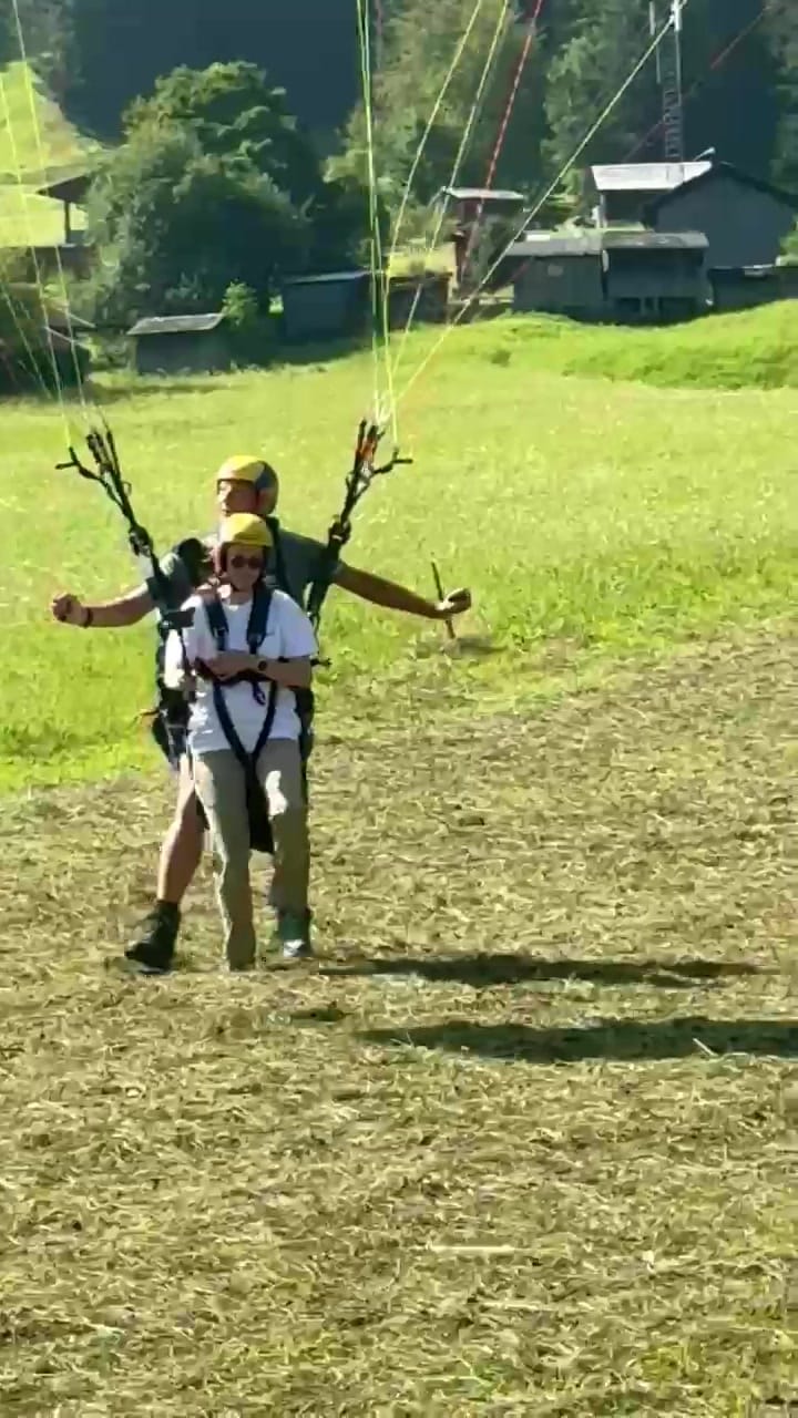 Nach der Landung: Pilot und Passagierin stehen lachend auf der Wiese, die Arme ausgebreitet.