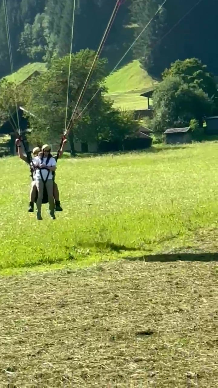 Standbild: Pilot und Passagierin setzen auf der Wiese auf, der Schirm steht noch über ihnen